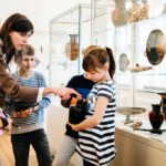 A young girl holding a replication of an artifact while on a field trip with her classmates to a museum.